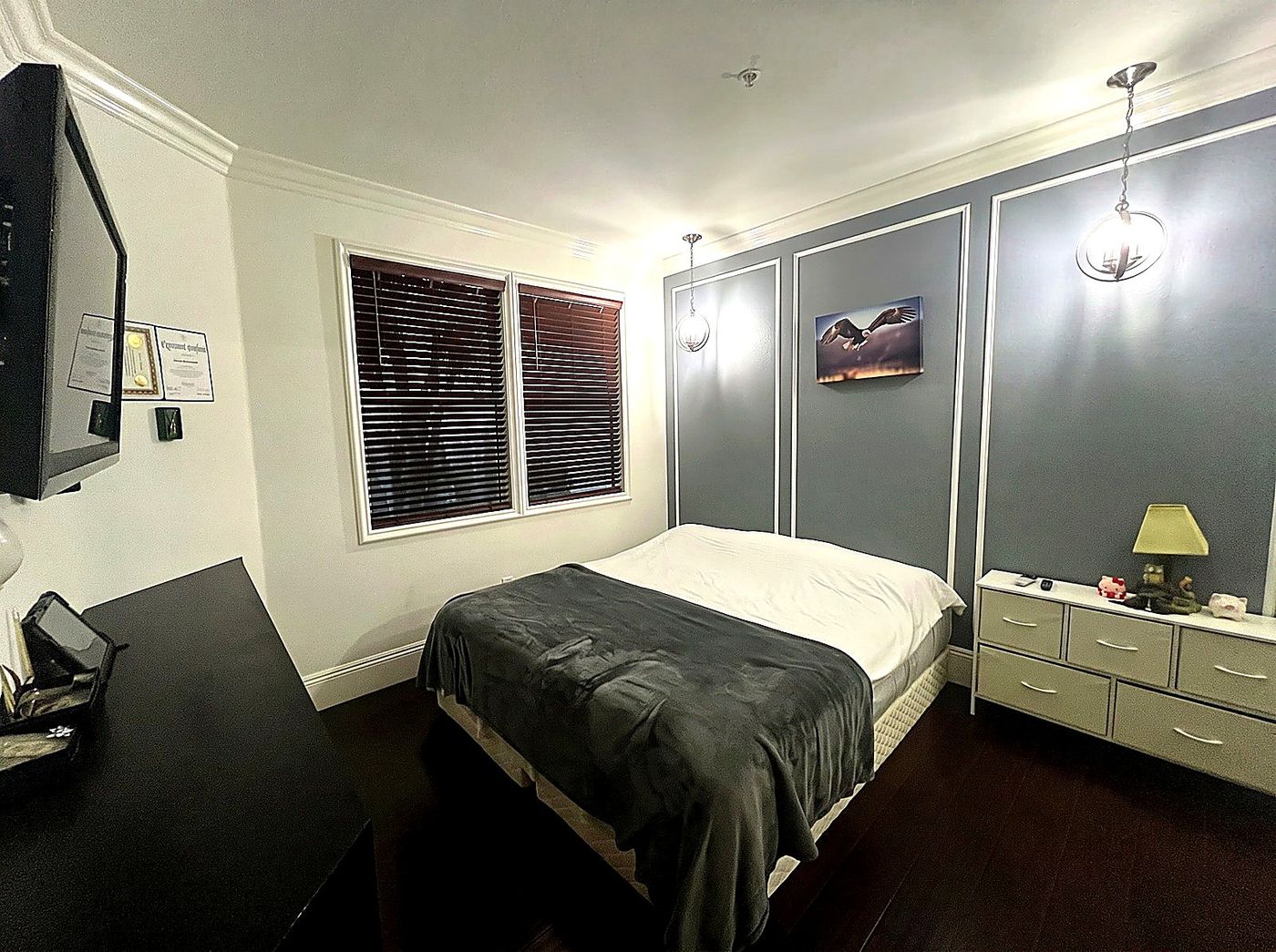 Bedroom featuring a slate blue accent wall with white wainscoting panels, pendant lighting, and dark hardwood floors.