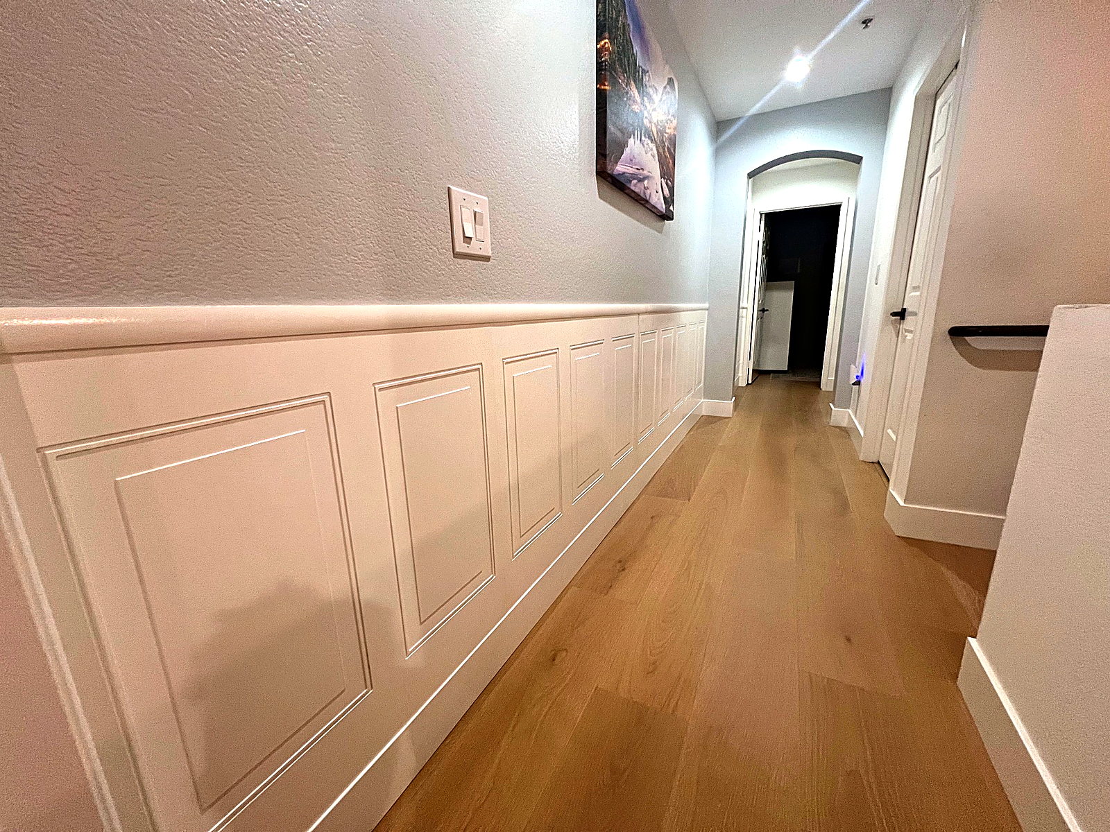 Clean hallway with custom white wall paneling, fresh paint, and warm wood flooring.