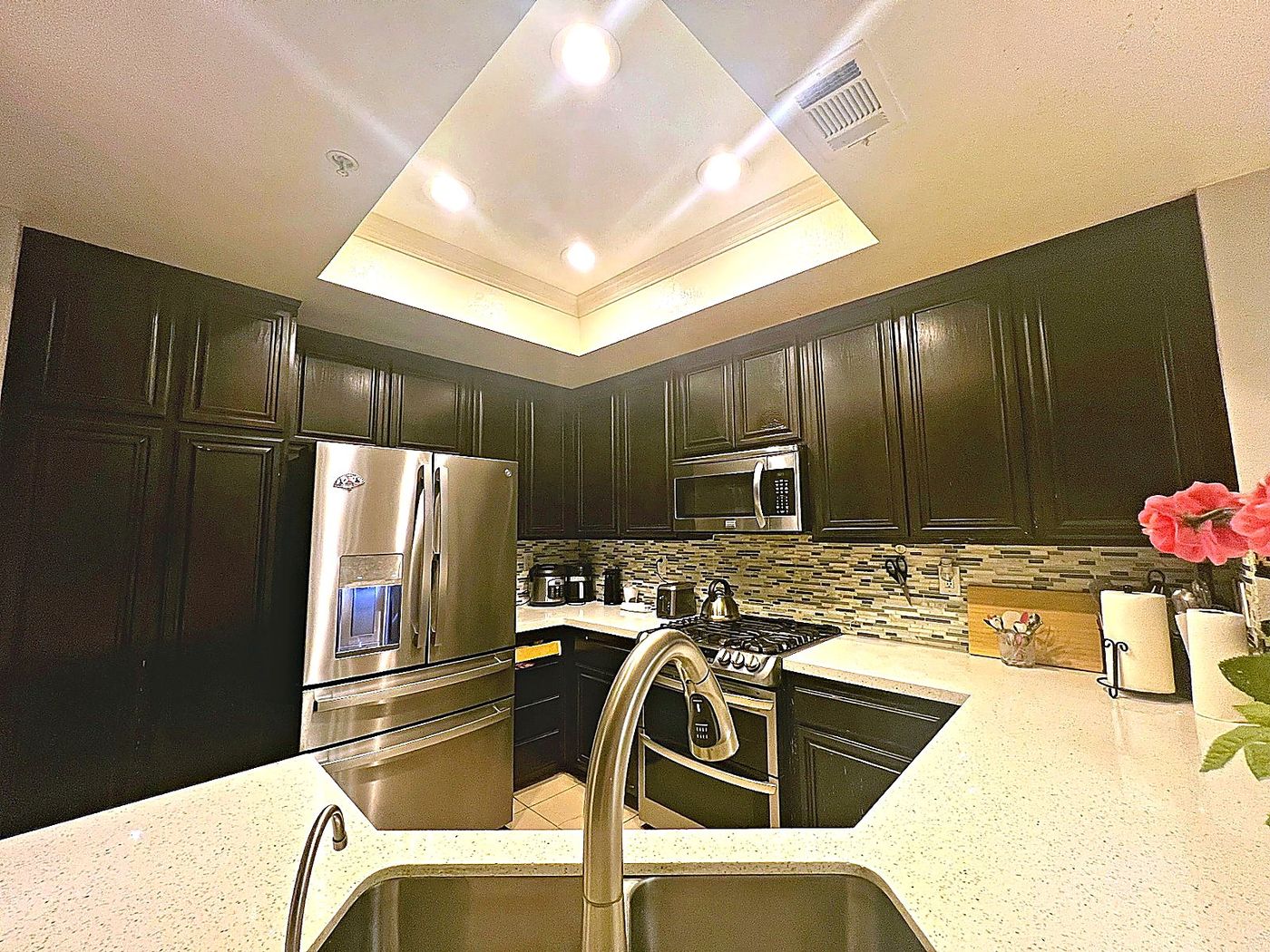 Kitchen remodel with dark cabinetry, bright counters, stainless appliances, and tray ceiling lighting.