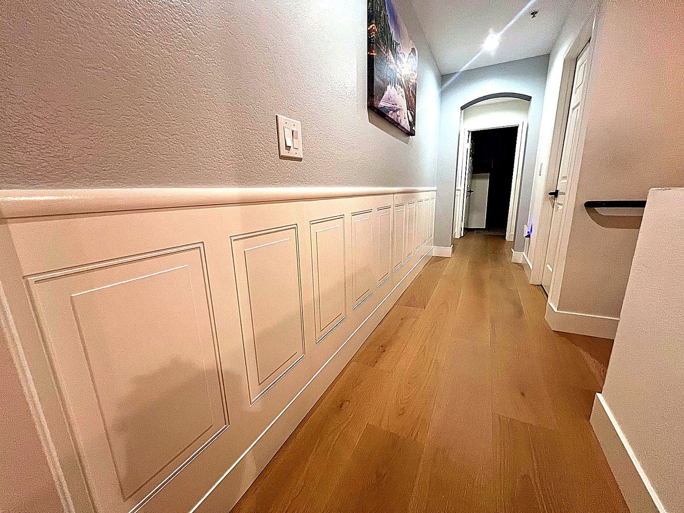 Clean hallway with custom white wall paneling, fresh paint, and warm wood flooring.