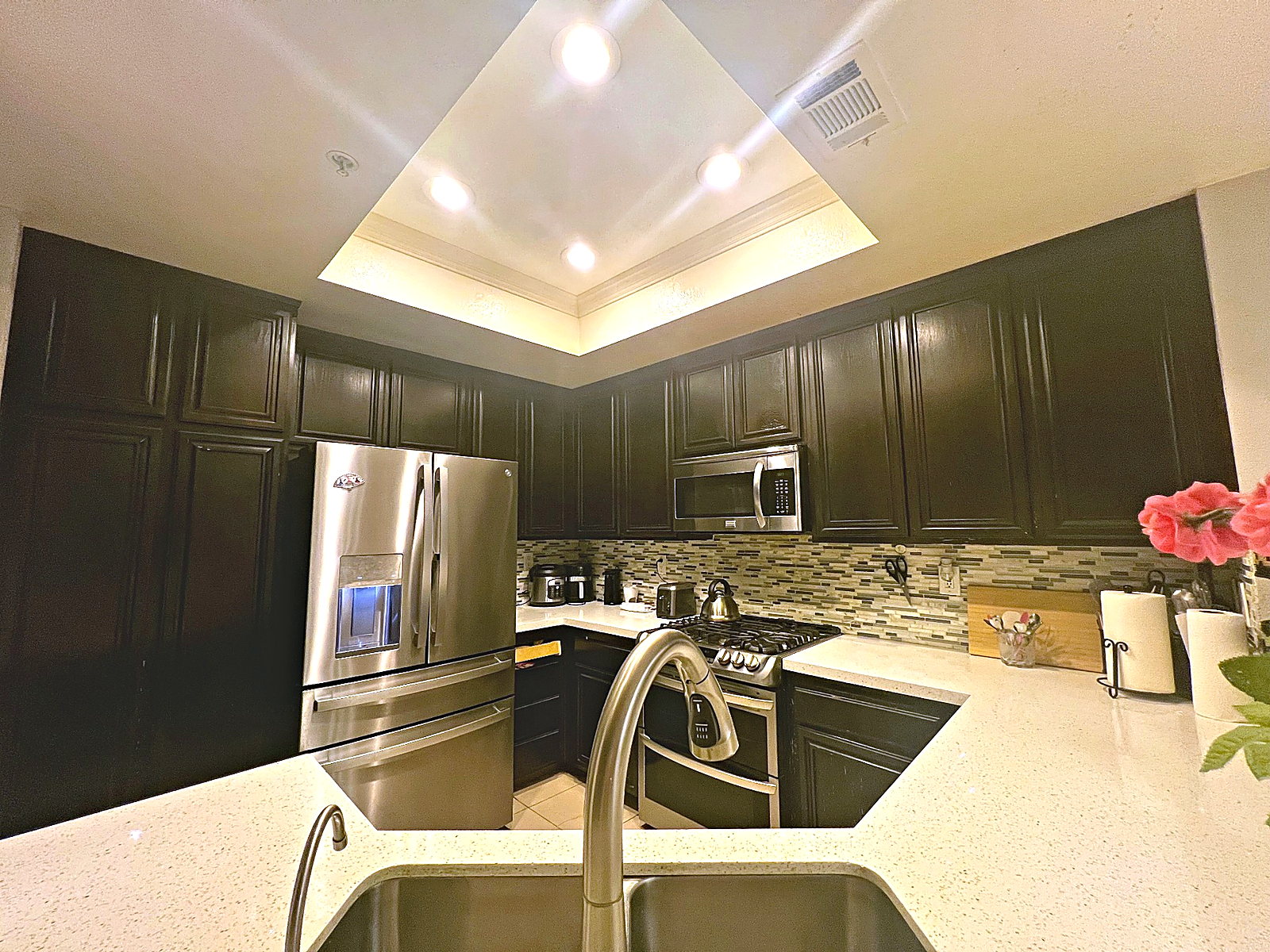 Kitchen remodel with dark cabinetry, bright counters, stainless appliances, and tray ceiling lighting.