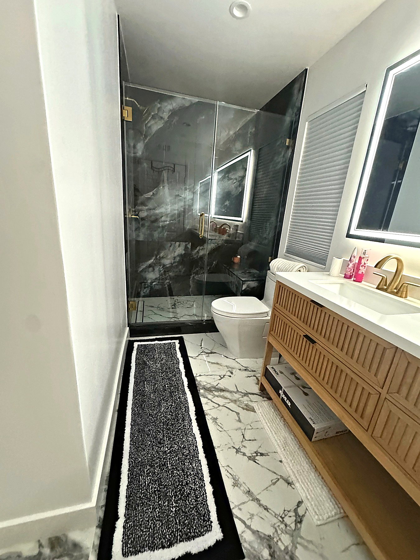 Bright bathroom remodel with marble-look floors, floating wood vanity, and glass shower enclosure.
