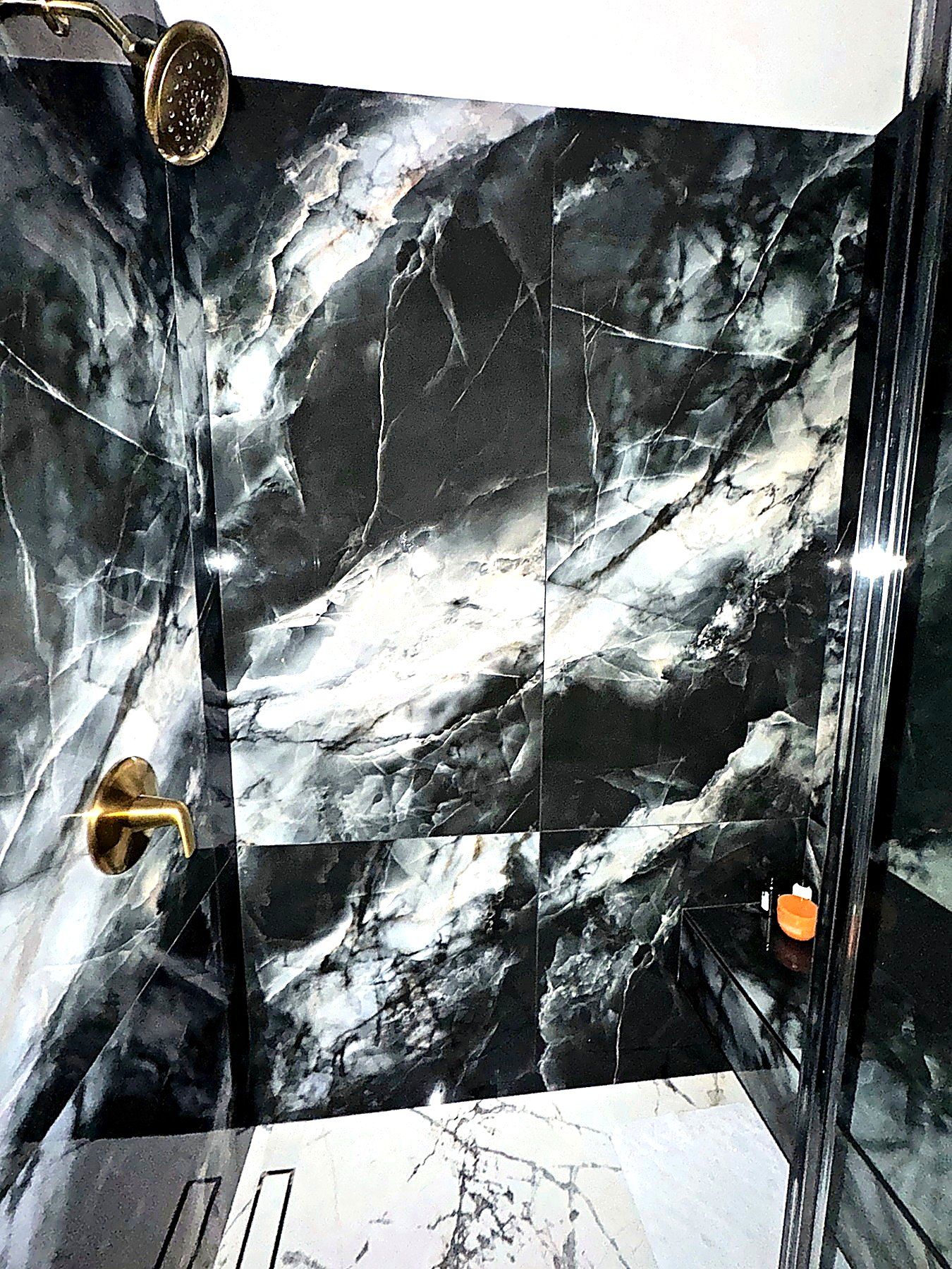Black marble-look shower surround with brass fixtures and dramatic stone veining.