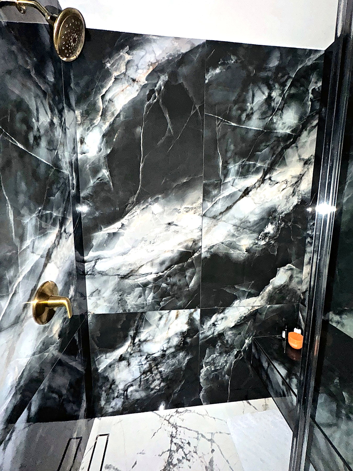 Black marble-look shower surround with brass fixtures and dramatic stone veining.