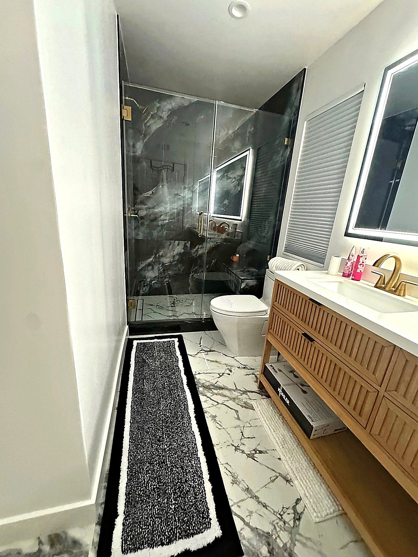 Bright bathroom remodel with marble-look floors, floating wood vanity, and glass shower enclosure.
