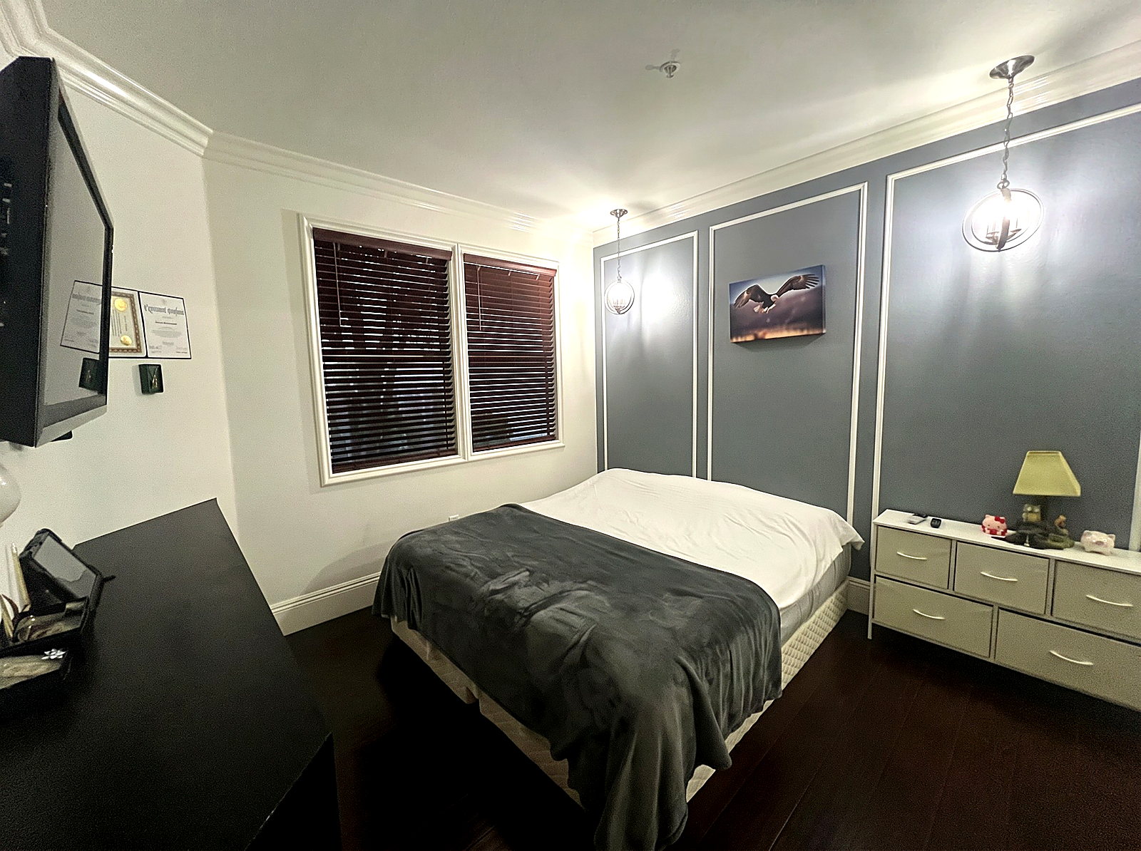 Bedroom featuring a slate blue accent wall with white wainscoting panels, pendant lighting, and dark hardwood floors.
