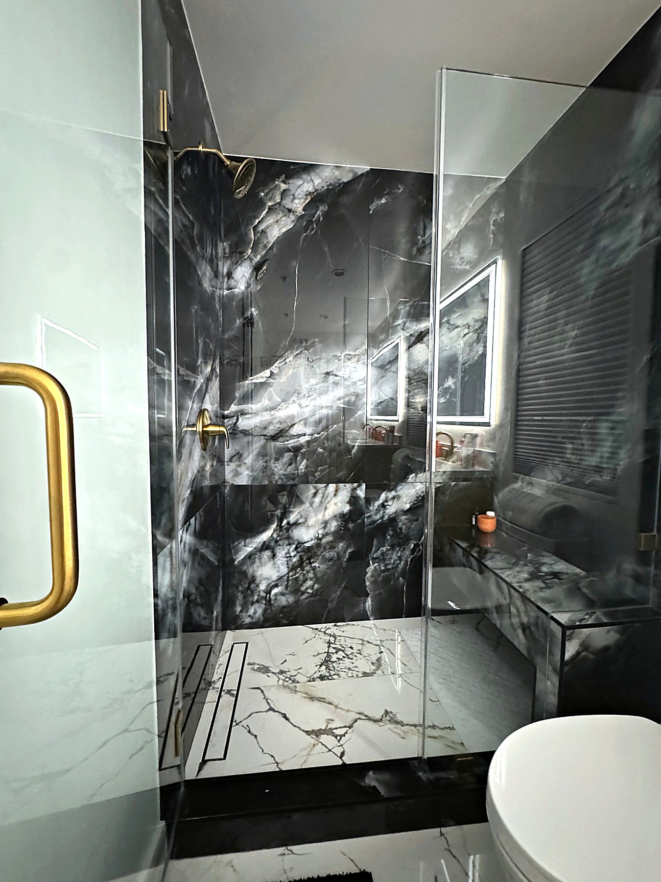 Modern walk-in shower with frameless glass, brass hardware, and polished large-format tile.